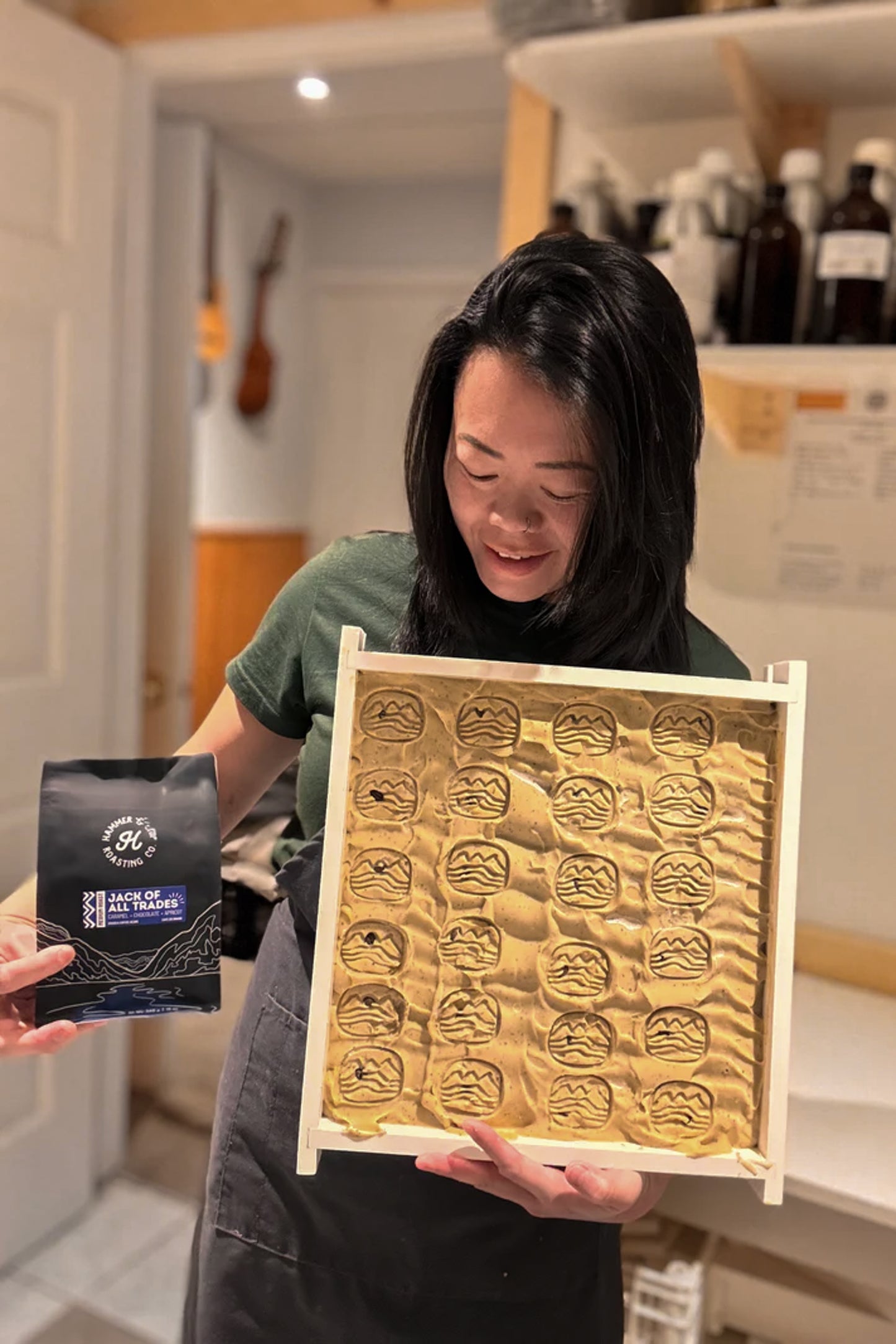 Person holding a uncut soap with intricate designs and a hammer & chip coffee bag.