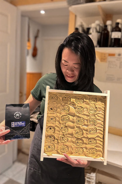 Person holding a uncut soap with intricate designs and a hammer & chip coffee bag.