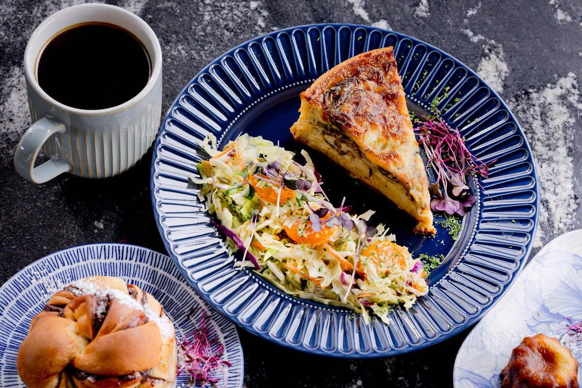 Plate with quiche slice and salad next to a cup of coffee on a dark surface